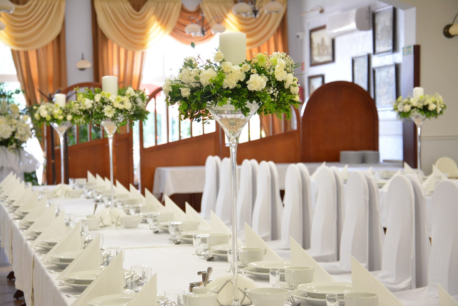 Sala weselna w Restauracji Kargul, długi stół z białymi obrusami, kompozycje z białych kwiatów i pokrowce na krzesłach