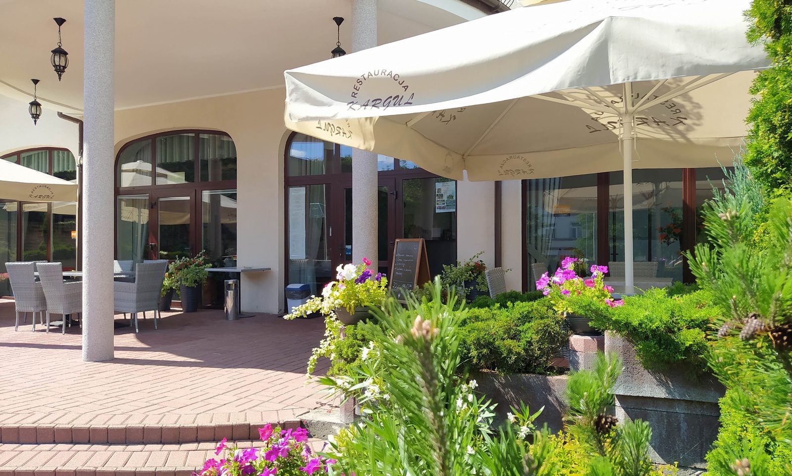 Taras restauracji z parasolami z nadrukiem Kargul i wiklinowymi fotelami